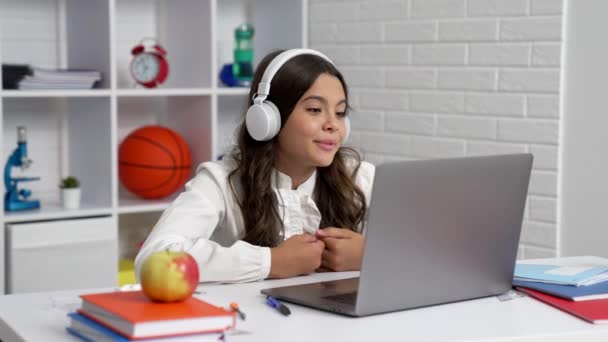 ノートパソコンと通信で学校のオンラインレッスンでヘッドフォンの勉強をしている笑顔の女子学生 - 映像、動画