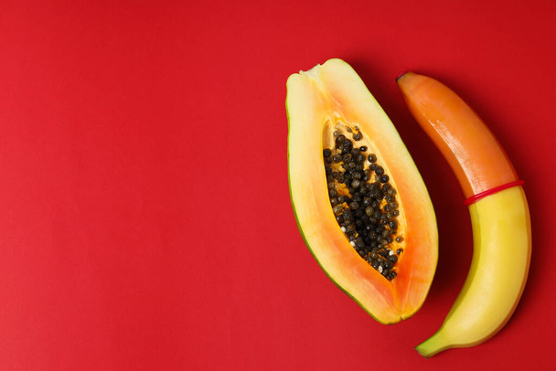 Papaya e banana con preservativo su sfondo rosso - Foto, immagini