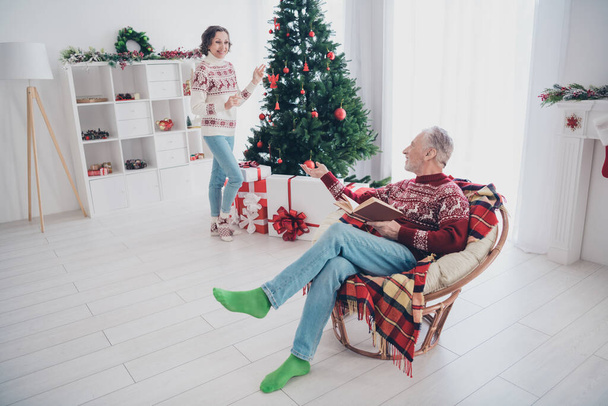 Photo of charming cute age couple dressed print pullovers enjoying book decorating tree smiling indoors room home house - Zdjęcie, obraz