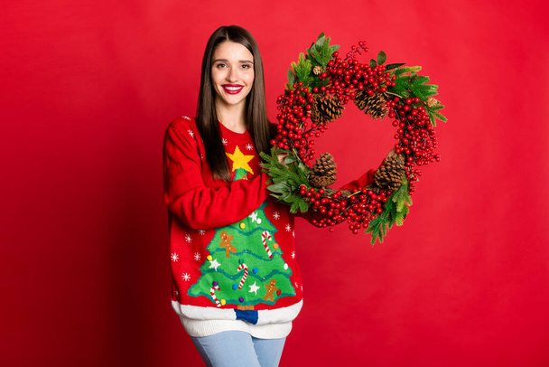 Portrait of attractive cheerful girl holding in hands wreath christmastime isolated over bright red color background - Фото, изображение