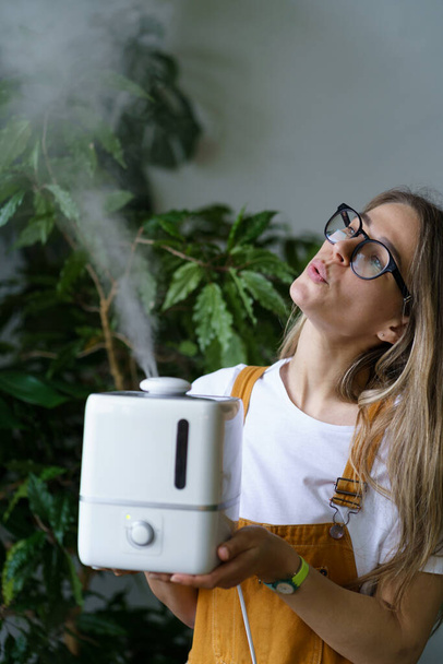 Giovane donna giardiniere tenere umidificatore d'aria nel giardino interno per salvare piante d'appartamento durante la stagione di riscaldamento - Foto, immagini