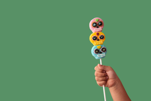 Kid hand holding candy skull lollipop on green background - Photo, Image