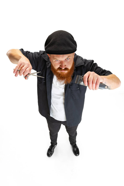 High angle view of red bearded man, barber or hair cutter in black cap isolated on white studio background. Holding his working equipment. - Φωτογραφία, εικόνα