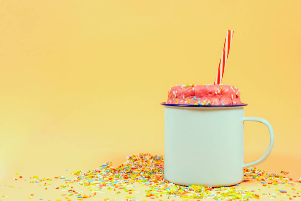 Un donut de fresa con salpicaduras de colores en una taza. - Foto, Imagen