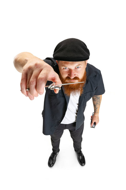 High angle view of red bearded man, barber or hair cutter in black cap isolated on white studio background. Holding his working equipment. - Foto, Bild