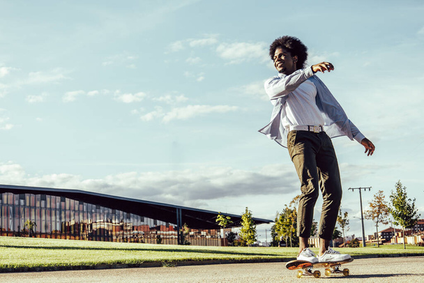 Picture of young dark skinned man wearing sunglasses and cap skateboarding. Against the nature background. - Foto, Imagem