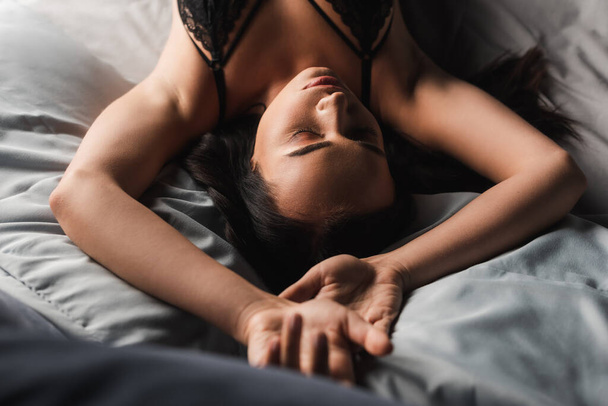 Top view of brunette woman in bra lying on bed  - Foto, imagen