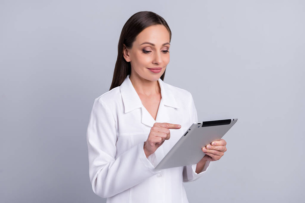 Retrato de atraente focado alegre enfermeira médico usando tablet procurando informações médicas isoladas sobre fundo de cor pastel cinza - Foto, Imagem