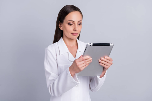 Portrait of attractive skilled focused nurse doctor using tablet reading prescription web isolated over grey pastel color background - 写真・画像