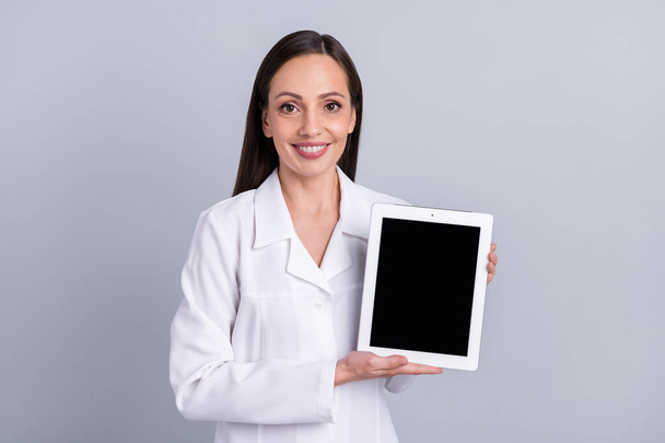 Foto van volwassen vrouw gelukkig positieve glimlach toon tablet touchscreen geneeskunde geïsoleerd over grijze kleur achtergrond - Foto, afbeelding