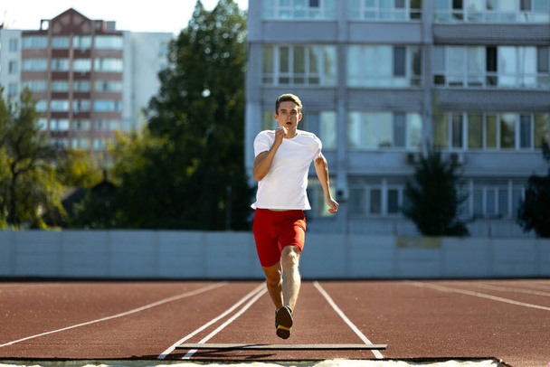 Young Caucasian man, male athlete, runner practicing alone at public stadium, sport court or running track outdoors. Summer sport games. - Фото, изображение