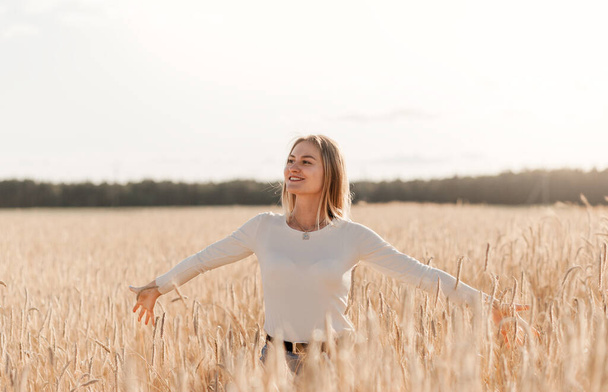 Una joven hermosa con falda de mezclilla camina por un campo de trigo en un día soleado - Foto, imagen