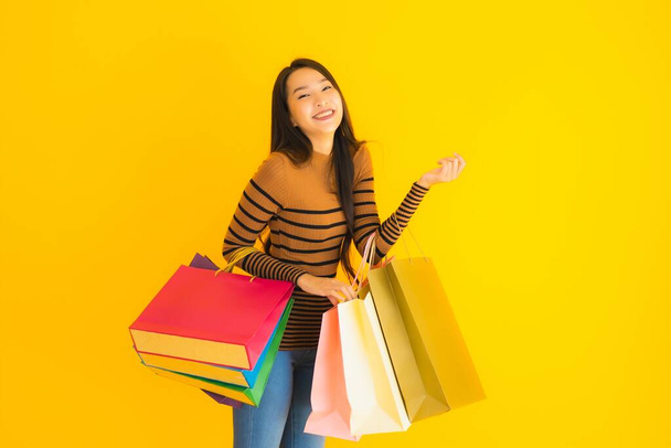 Porträt schöne junge asiatische Frau glücklich lächeln mit viel Farbe Einkaufstasche aus dem Kaufhaus auf gelbem Hintergrund isoliert - Foto, Bild