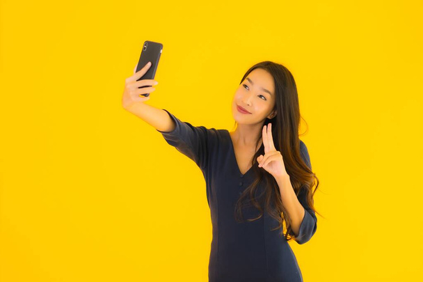 Портрет красивої молодої азіатки зі смартфоном або мобільним телефоном на жовтому ізольованому фоні
 - Фото, зображення
