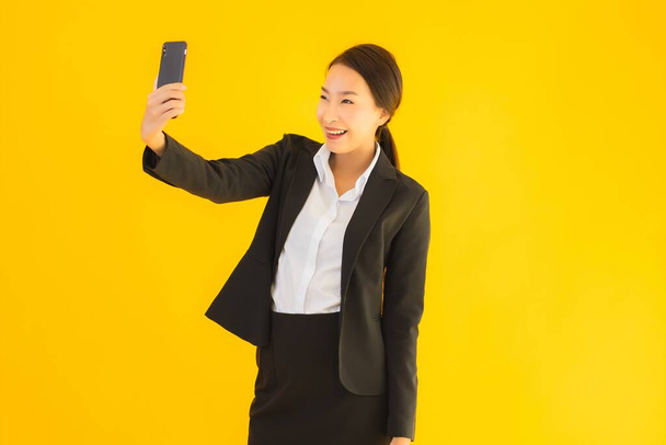 Portret mooie jonge business aziatische vrouw met slimme mobiele telefoon en koffiekopje op geel geïsoleerde achtergrond - Foto, afbeelding