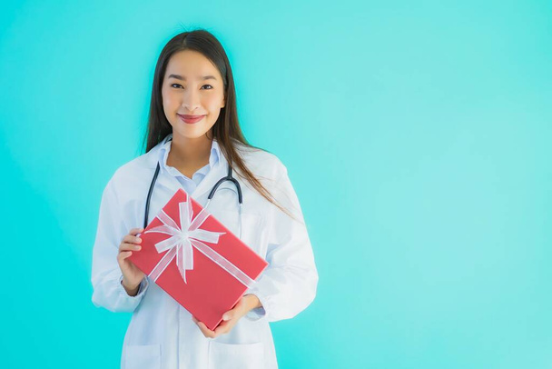 Retrato hermosa joven asiática médico mujer con caja de regalo en azul aislado fondo
 - Foto, imagen