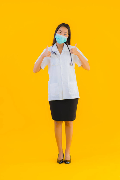 Portrait beautiful young asian doctor woman with mask for protect covid19 or coronavirus on yellow isolated background - Photo, Image