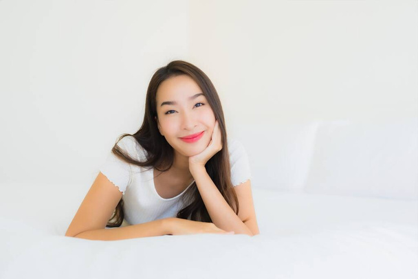 肖像画美しい若いアジアの女性リラックス幸せな笑顔でベッドの上に白い枕毛布インテリアのベッドルーム - 写真・画像