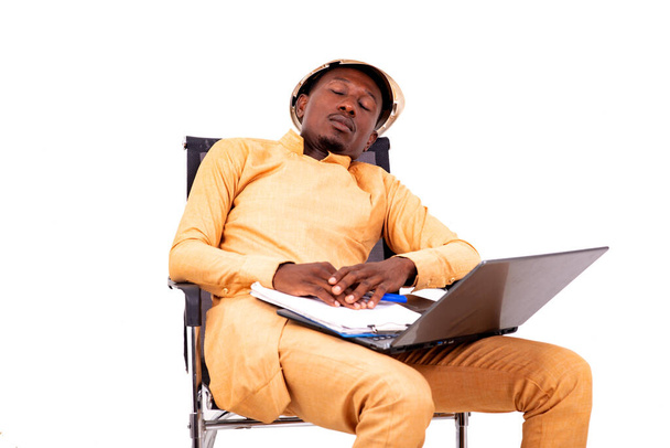 joven arquitecto cansado hombre de negocios sentado en la silla con el ordenador portátil y portapapeles mientras duerme. - Foto, imagen