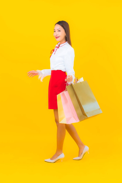 Portrét krásná mladá asijská žena s nákupní taškou a kreditní kartou na žlutém pozadí - Fotografie, Obrázek