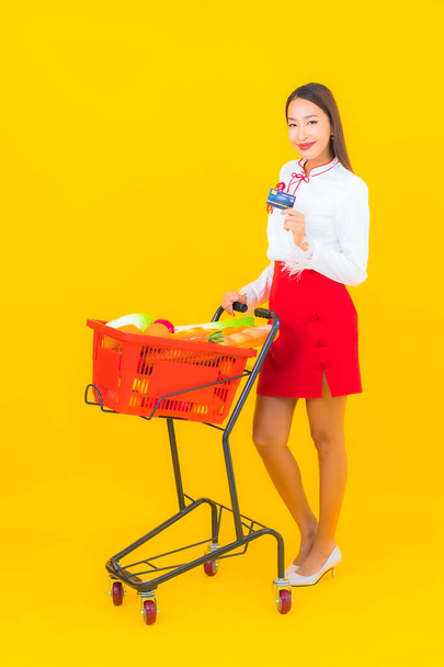 Portrait beautiful young asian woman with grocery basket from supermarket on yellow background - Photo, image