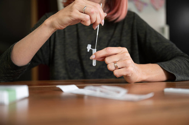 Front view of a woman making rapid self home covid 19 test - dipping cotton swab in a solution. - 写真・画像