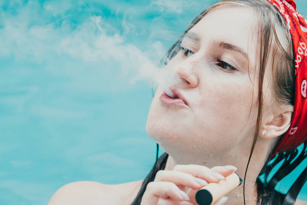 Woman smoking with electronic cigarette. Young woman smoking electronic cigarette in outdoors pool - Foto, Bild