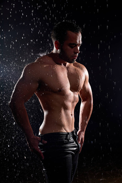 Handsome young man with naked torso posing at camera on black background. - 写真・画像
