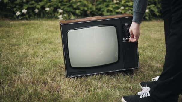 Man turns on old retro TV set standing on grass. Then person switches channels - Footage, Video