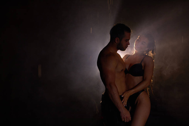 Apasionada pareja sensual posando en habitación estudio oscuro, luz y lluvia en el fondo - Foto, Imagen