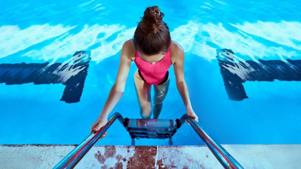 Young slim fitness swimmer woman in swimsuit using pool ladder during swimming in sports pool in leisure centre. Do sport and healthy lifestyle  - Foto, imagen