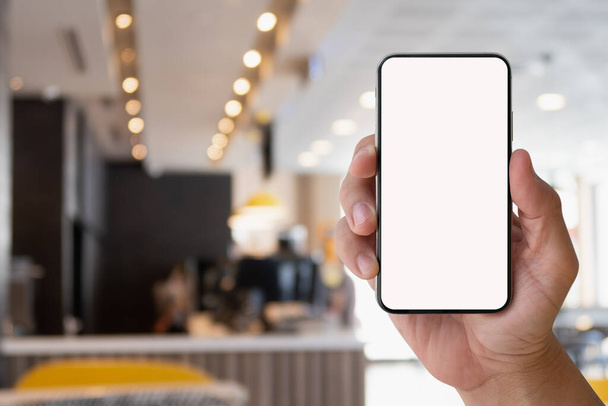 Ruční držení chytrý telefon zařízení s prázdnou obrazovkou v rozmazané kavárně nebo kavárně pozadí. - Fotografie, Obrázek