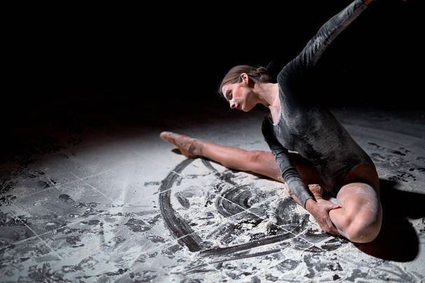 Гнучка балерина рухається витончено сидячи на підлозі в студії, в борошні
 - Фото, зображення