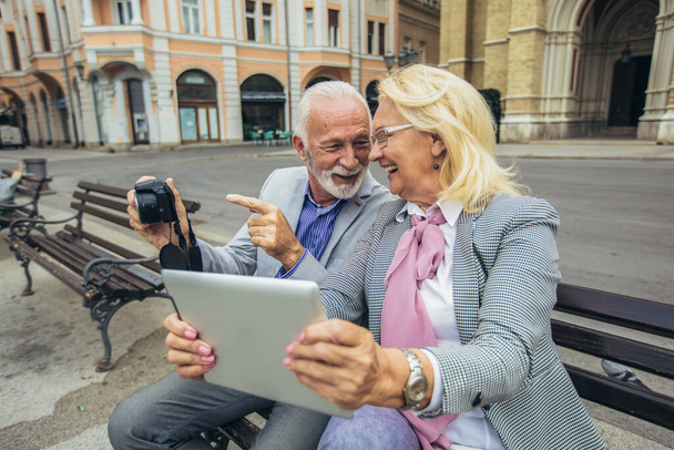  Coppia di anziani alla scoperta di una nuova città scattare foto su fotocamera retrò e tablet digitale. - Foto, immagini