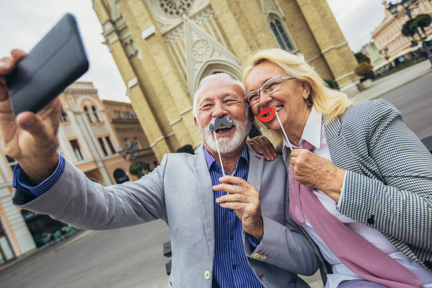 Feliz pareja de ancianos tomando una selfie juntos en la ciudad y divirtiéndose. - Foto, imagen
