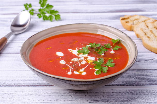 Red puree soup with cream, oil and parsley leaves on a light wooden background. Selective focus. - Photo, Image