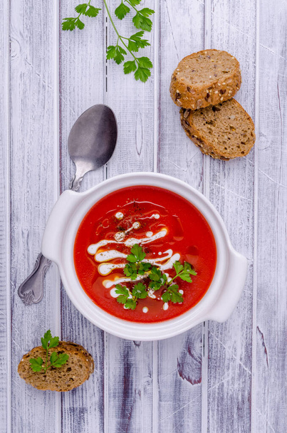 Rote Püree-Suppe mit Sahne, Öl und Petersilienblättern auf hellem Holzgrund. Selektiver Fokus. - Foto, Bild