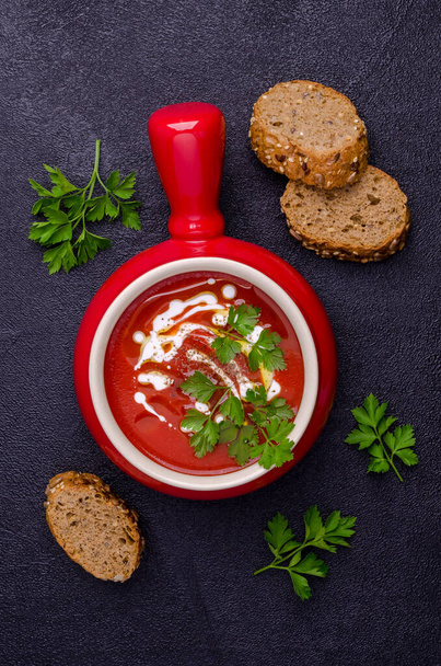 Red puree soup with cream, oil and parsley leaves on a black stone background. Selective focus. - Photo, Image