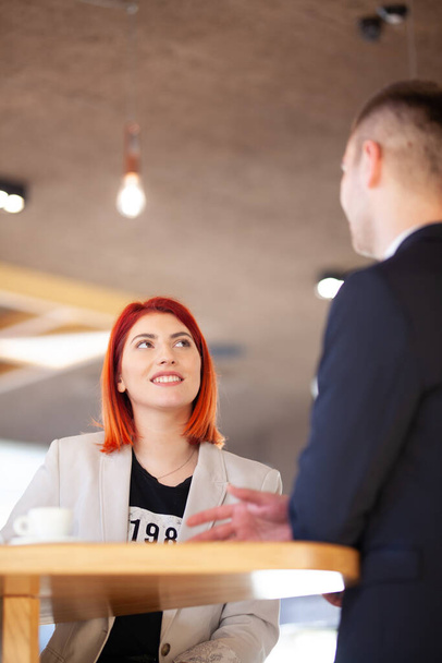 Two colleagues having a meeting at a modern cafe interior. Red hair girl and man in a suit. - Foto, imagen