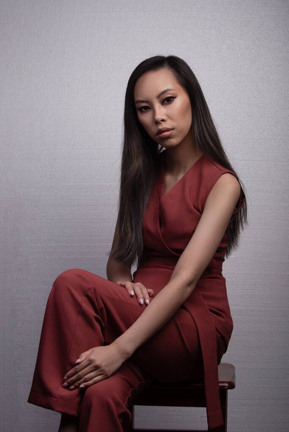 Jovem mulher asiática em traje vermelho sentado na cadeira no estúdio - Foto, Imagem