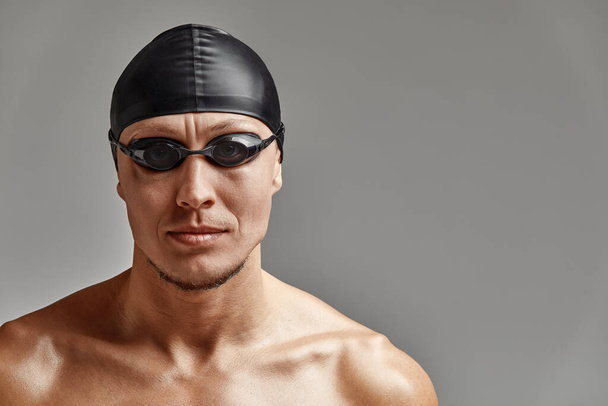 Portret van een zwemmer met pet en masker, halflang portret, jonge atleet zwemmer met pet en masker om te zwemmen, kopieën van ruimte, grijze achtergrond - Foto, afbeelding