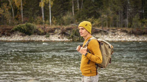 Erkek gezgin, bir sonbahar ormanının arka planına karşı kıyıda büyük taşlarla hızlı bir dağ nehri boyunca yürüyor. Yürüyüş ve seyahat kavramı - Fotoğraf, Görsel
