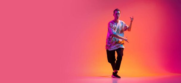 Young boy dancing hip-hop in stylish colorful clothes isolated over gradient background in neon light. Flyer - Φωτογραφία, εικόνα