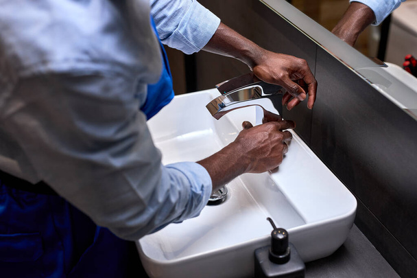 Close up of unrecognizable black plumbers hand trying to open a water tap at bathroom - 写真・画像