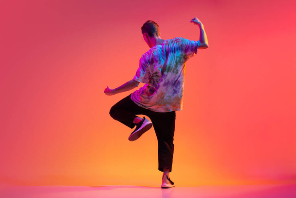 Back view of young stylish man dancing hip-hop isolated over colorful gradient background in neon light. - Foto, imagen