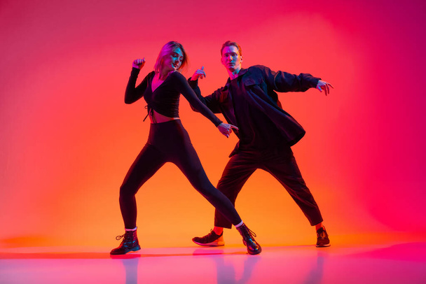 Attractive young man and woman dancing hip-hop isolated on gradient pink studio background in neon light - Fotografie, Obrázek