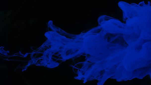 Drops of blue ink in water. Blue watercolor paints in water on a black background. Awesome abstract background. Beautiful wallpaper for your desktop. Blue cloud of ink on a black background. - Фото, изображение