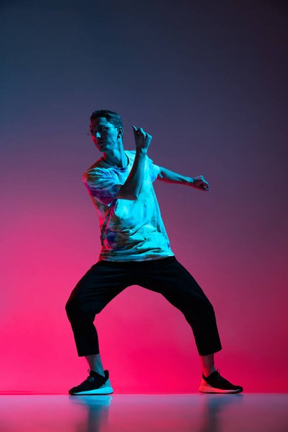 Vertikales Porträt einer dynamischen Hip-Hop-Tänzerin, die isoliert über einem Gradienten in rosa lila Hintergrund im Neonlicht übt - Foto, Bild