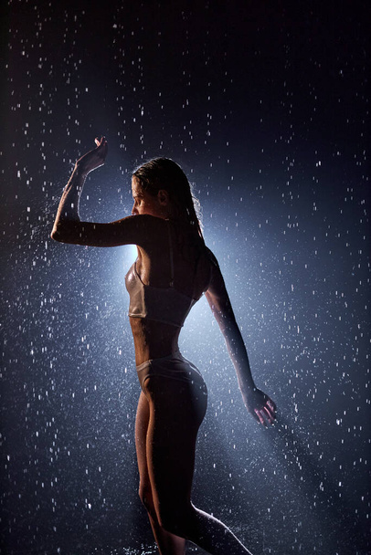 professional female performer is dancing under rain in darkness, sexy and sensual - Photo, Image