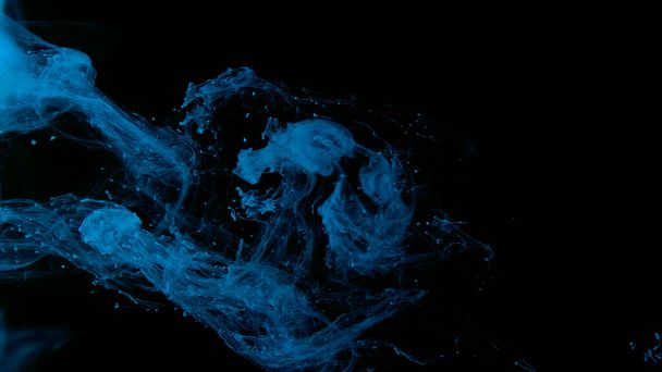 Drops of blue ink in water. Blue watercolor paints in water on a black background. Awesome abstract background. Beautiful wallpaper for your desktop. Blue cloud of ink on a black background. - Foto, Imagen